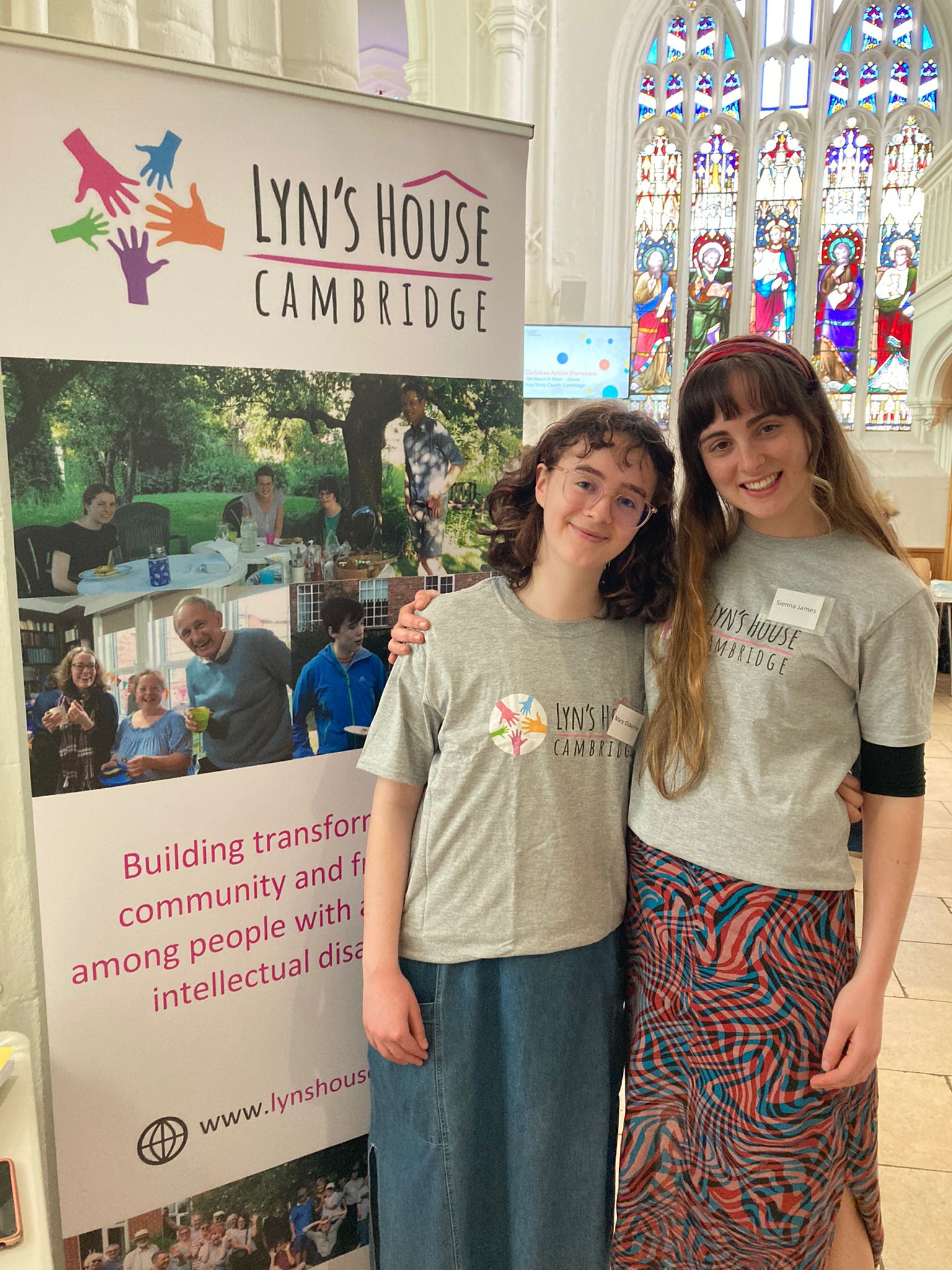Two people standing beside a Lyn's House banner