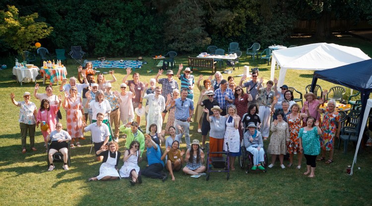 A large group of people of different abilities gathered on a lawn on a sunny day, facing the camera.