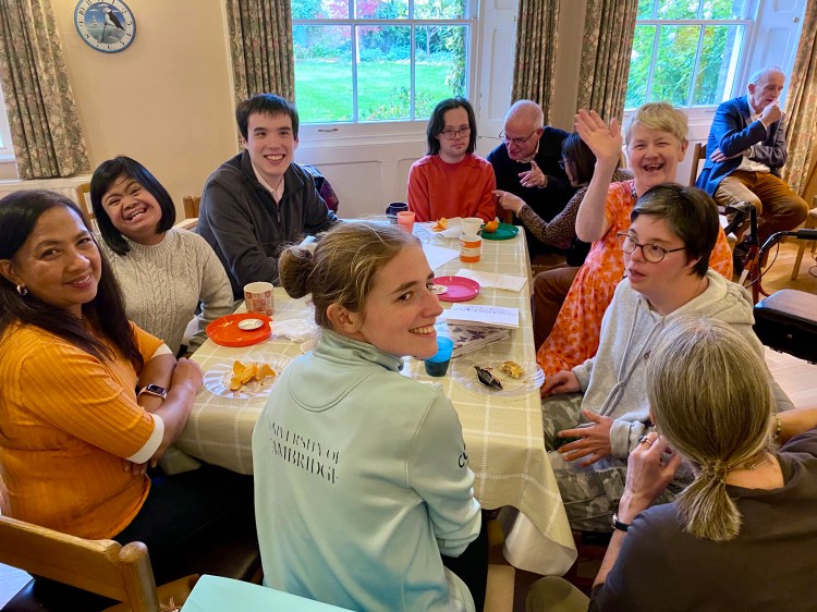A group of differing abilities around a table with food; some smiling.