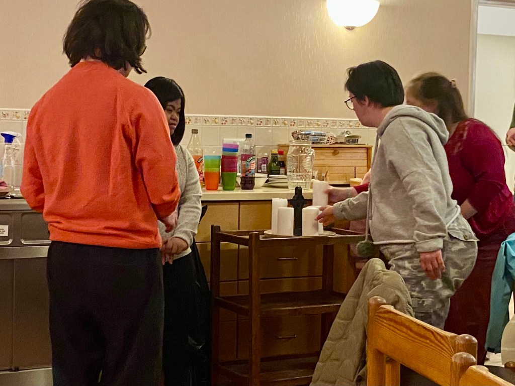 Four people are lighting candles set around a small cross
